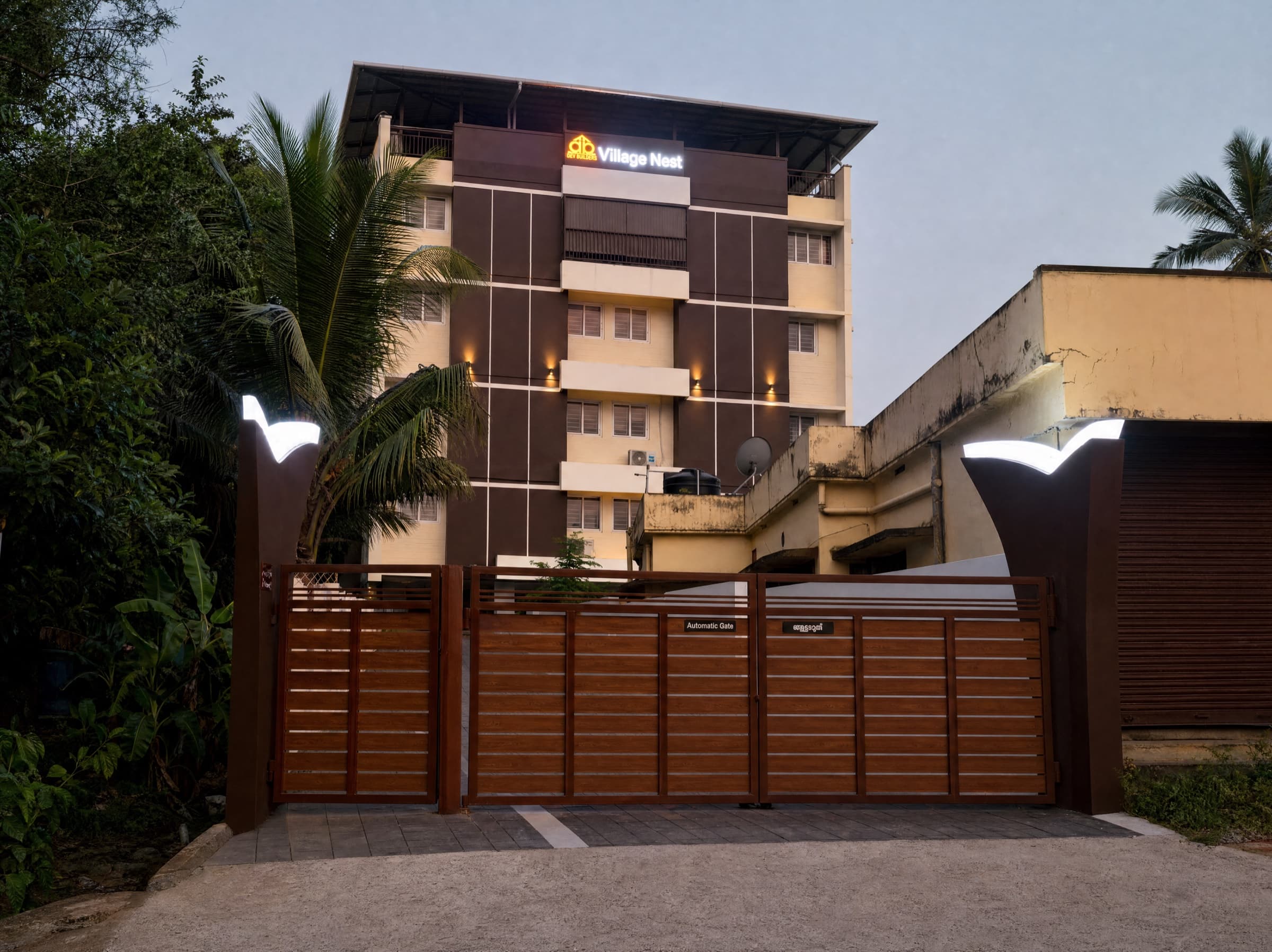 Village Nest — the gated entrance at dusk, sign lit above the facade